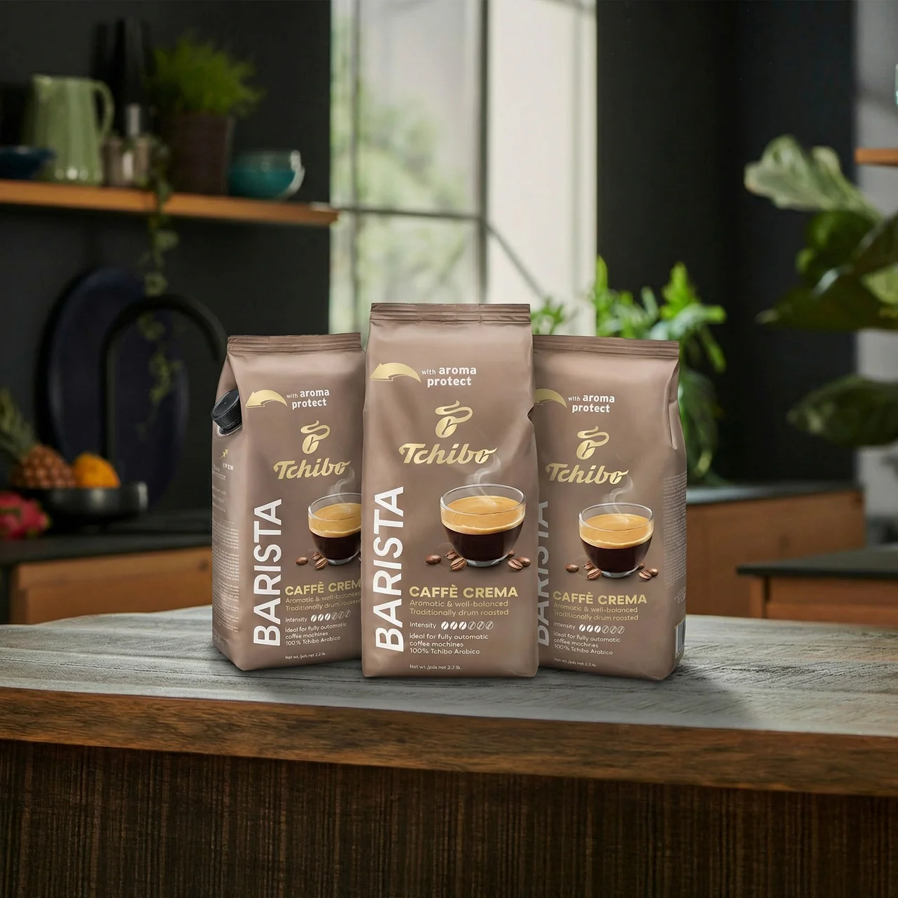 Trzy opakowania Tchibo Barista Caffè Crema na drewnianym blacie przed oknem.
