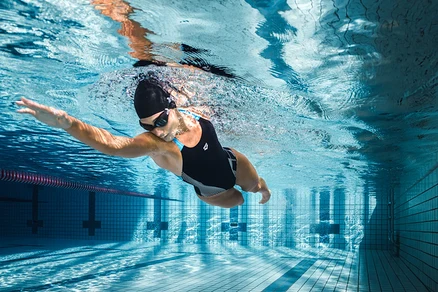 Kobieta płynie pod wodą w basenie w czarnym kostiumie kąpielowym arena Feel Lily Swim Pro Back.