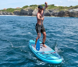 Mężczyzna wiosłuje na niebieskiej desce Aqua Marina SUP »Beast« 10'6" na morzu.