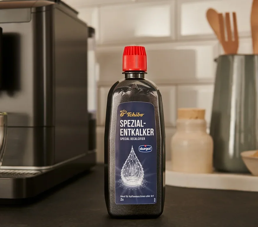 Czarna butelka specjalistycznego odkamieniacza durgol® 400 ml stoi na blacie obok ekspresu do kawy.