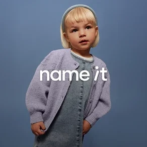 Małe dziecko z blond włosami i niebieską opaską na głowie ma na sobie dżinsowe ogrodniczki i liliowy kardigan na tle niebieskiego tła.
