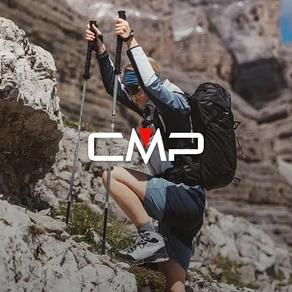 Kobieta z plecakiem i kijkami trekkingowymi wspina się po skałach. Ma na sobie buty trekkingowe, szorty i kurtkę.