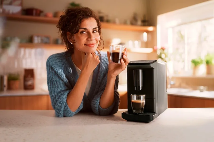 Kobieta trzyma filiżankę kawy obok ekspresu do kawy.