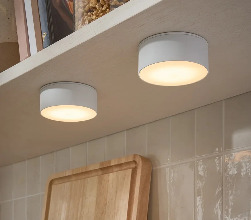 Dwie wielofunkcyjne lampy LED przymocowane do spodu półki. Na półce stoją słoiki z orzechami i książki.