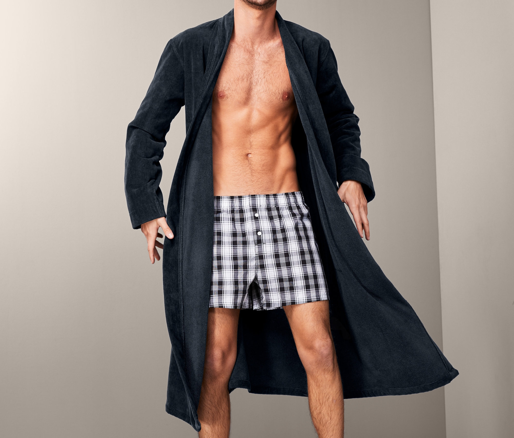 Mężczyzna pozuje w granatowym welurowym szlafroku i bokserkach w kratę.