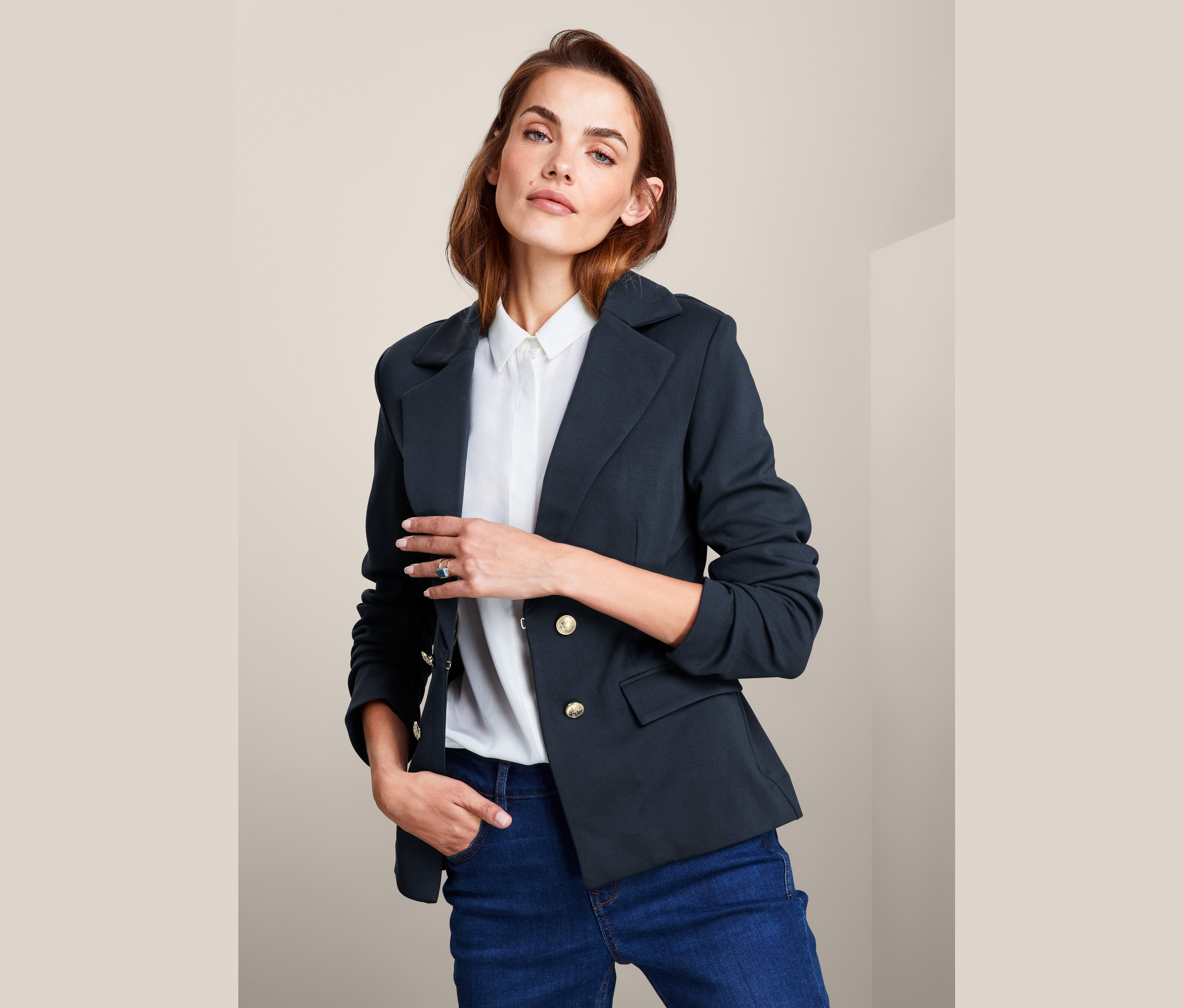 Kobieta pozuje w żakiecie z dzianiny dresowej, białej koszuli i dżinsach.