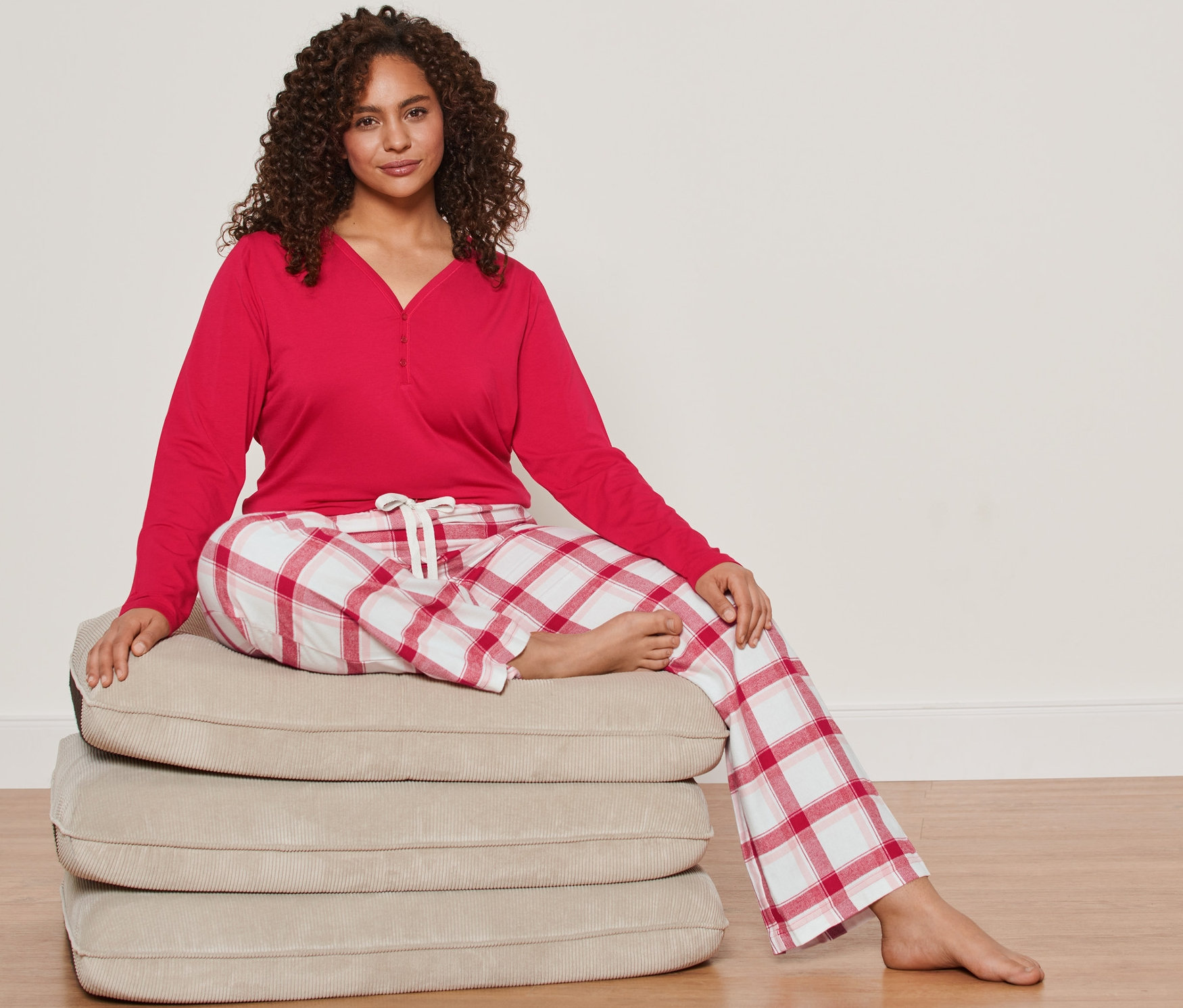 Kobieta siedzi na stosie poduszek, ubrana w piżamę flanelową.