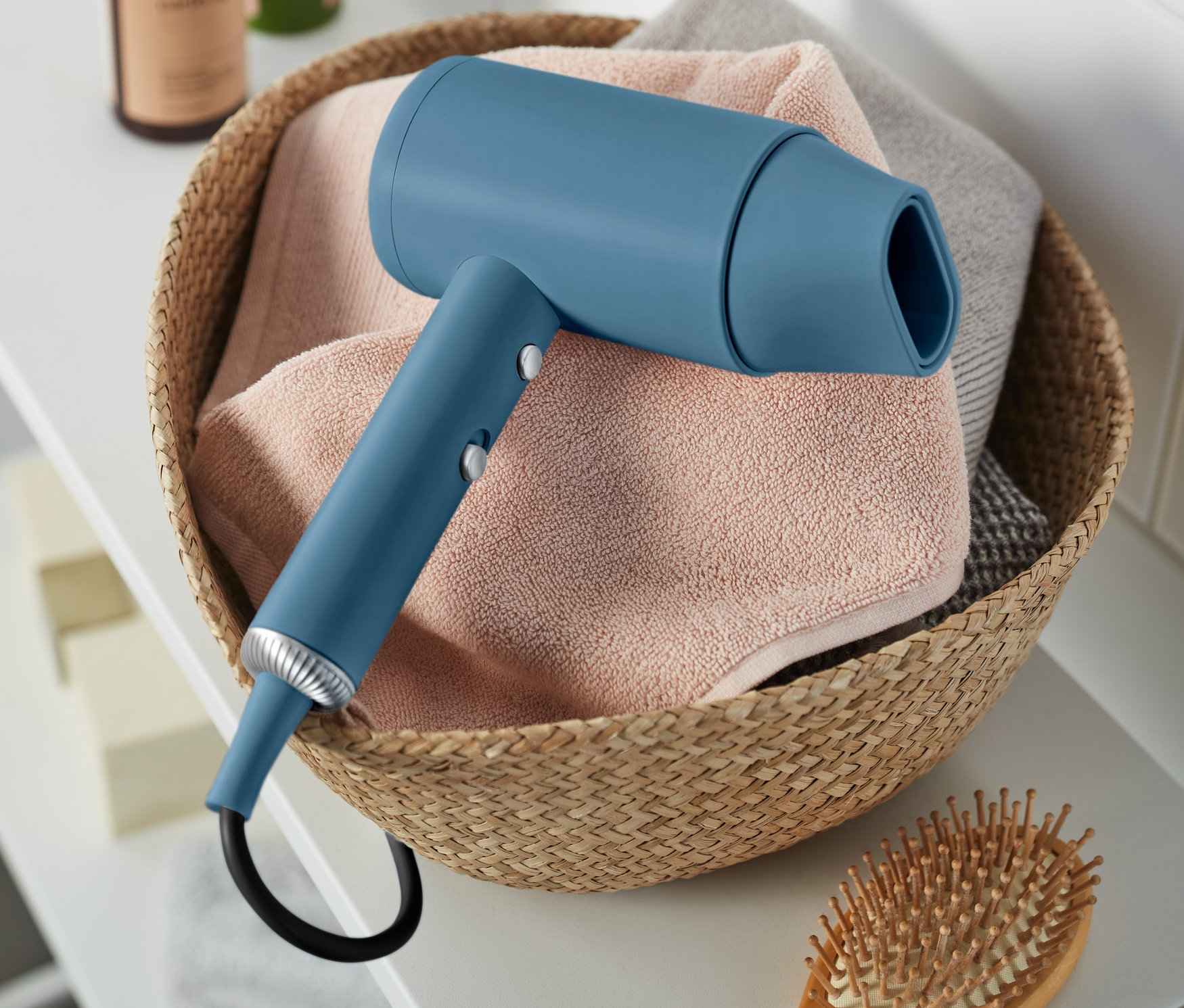 Niebieska suszarka do włosów w koszu z ręcznikami obok drewnianej szczotki do włosów.
