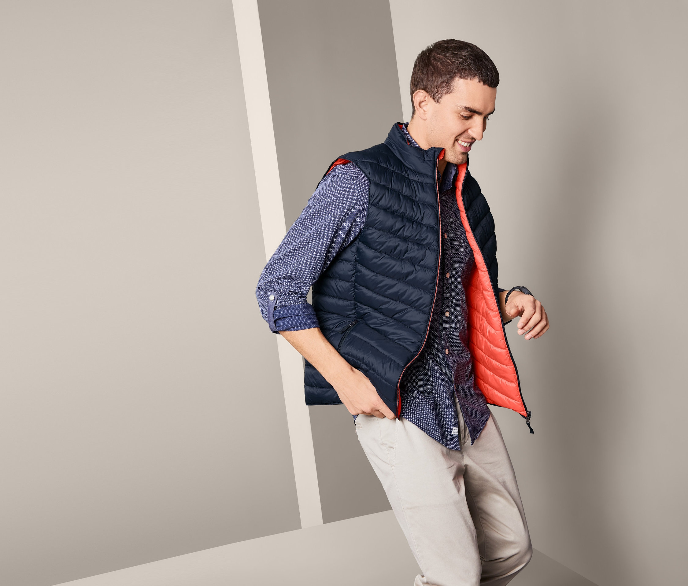 Mężczyzna w niebieskiej koszuli i beżowych spodniach pozuje w męskiej, dwustronnej kamizelce pikowanej.