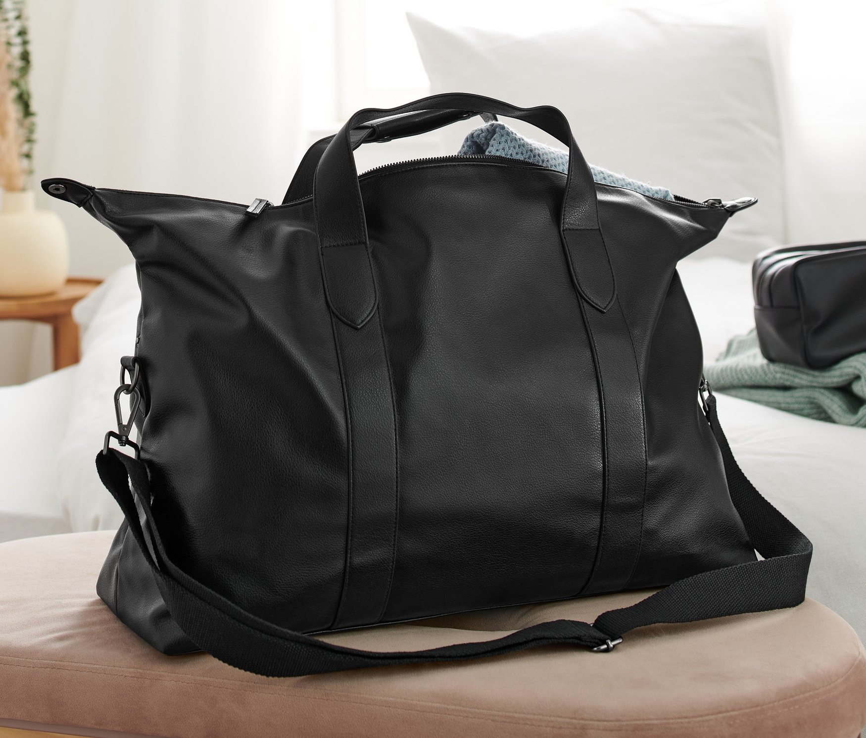 Czarna torba leży na beżowej ławce w sypialni.