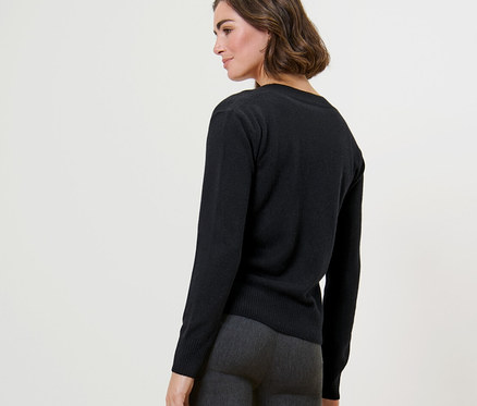 Kobieta pozuje w czarnym kardiganie z delikatnej dzianiny z kaszmirem i szarych spodniach.