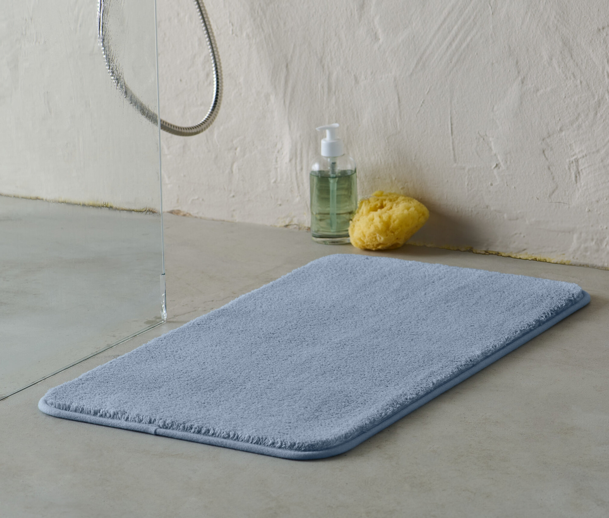 Niebieska mata łazienkowa o wymiarach ok. 70 x 40 cm leży na podłodze obok prysznica.