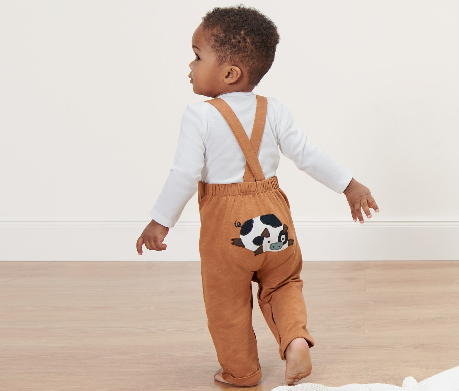 Małe dziecko w ogrodniczkach z naszywką leżącej krowy.