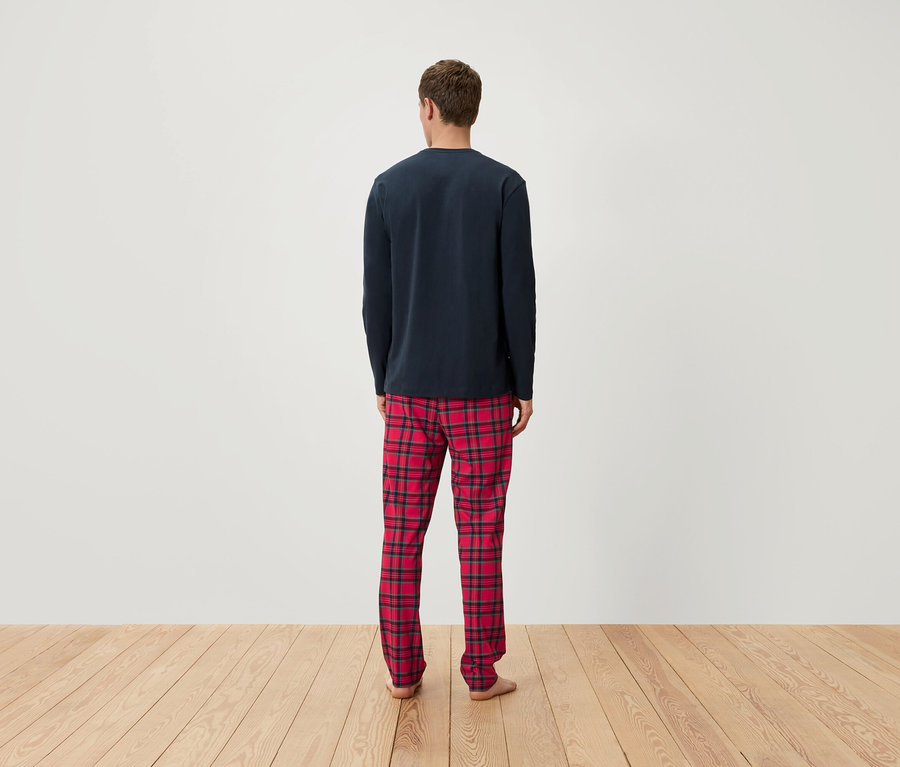 Mężczyzna tyłem do kamery ma na sobie granatową koszulkę z długim rękawem od piżamy i czerwoną piżamę w kratę.