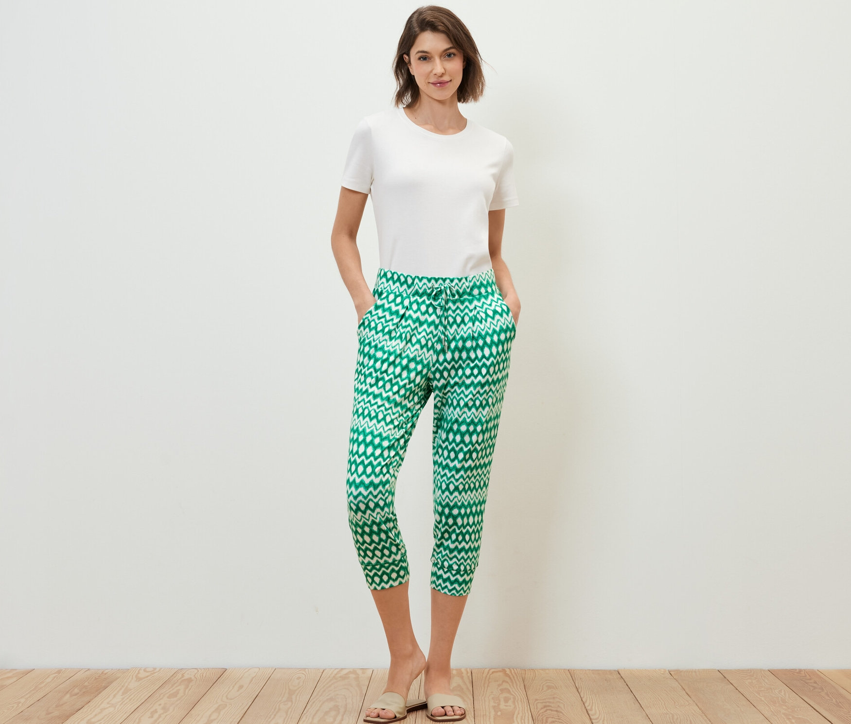 Kobieta stoi z rękami w kieszeniach w spodniach dżersejowych o długości 3/4.