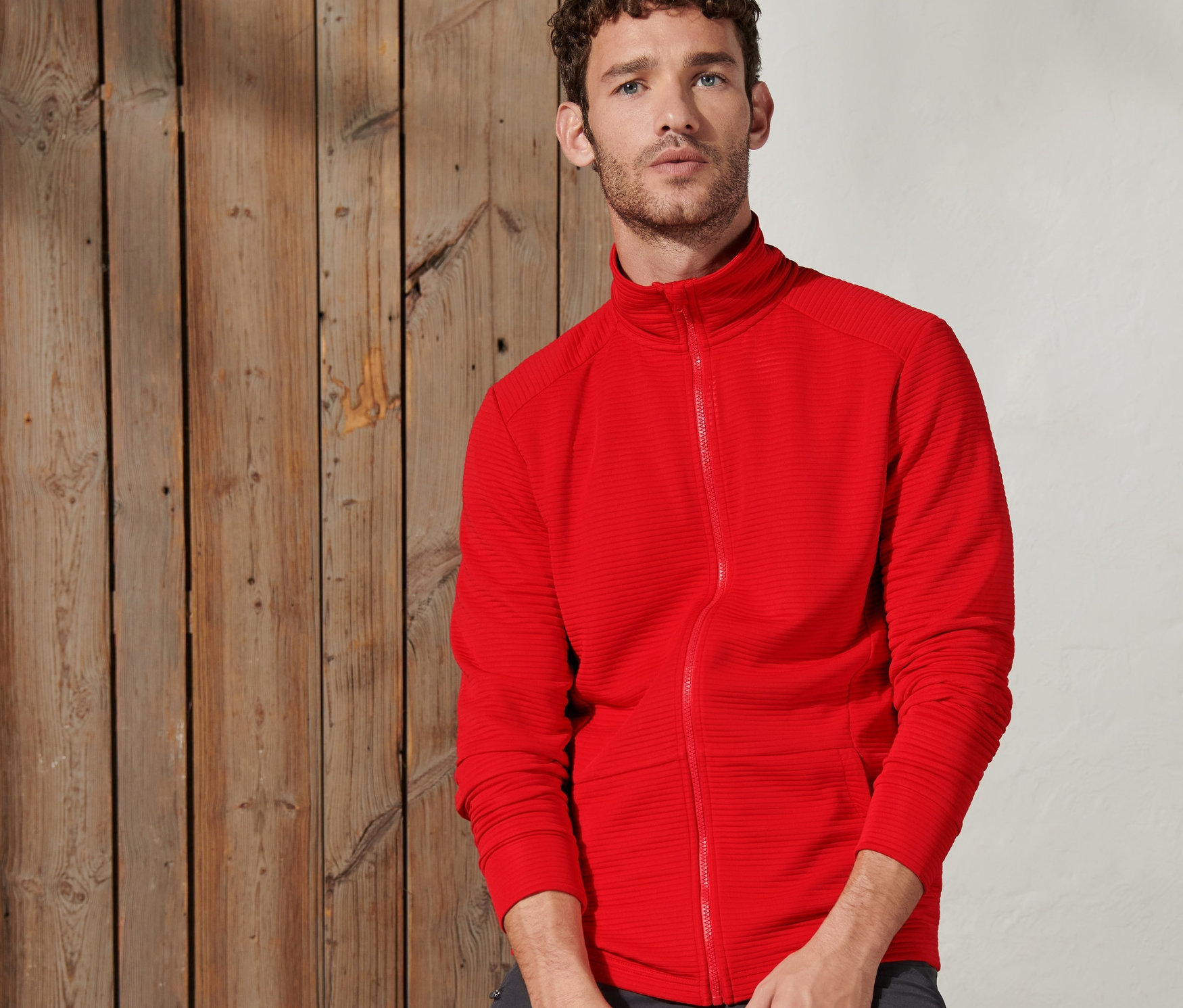 Mężczyzna siedzi na drewnianej belce i ma na sobie czerwono-pomarańczową kurtkę funkcyjną.