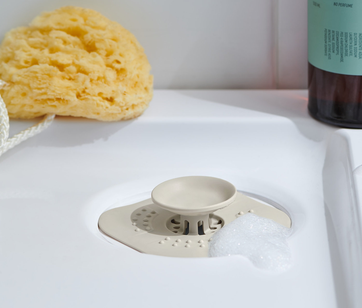 Sitko-korek do odpływu leży w umywalce, obok niego gąbka do mycia, a za nim butelka żelu do mycia ciała.