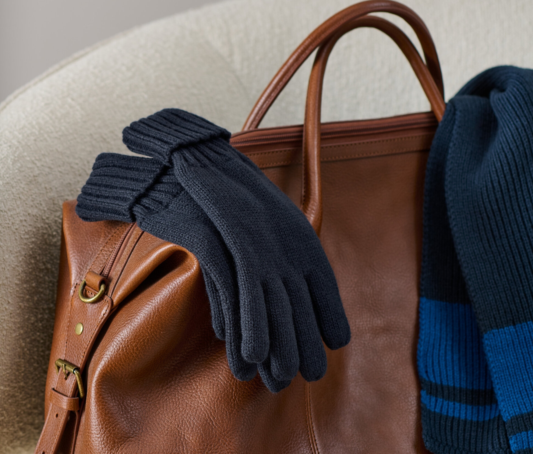 Rękawiczki z dzianiny leżą na brązowej skórzanej torbie wraz z dzianinowym szalikiem.