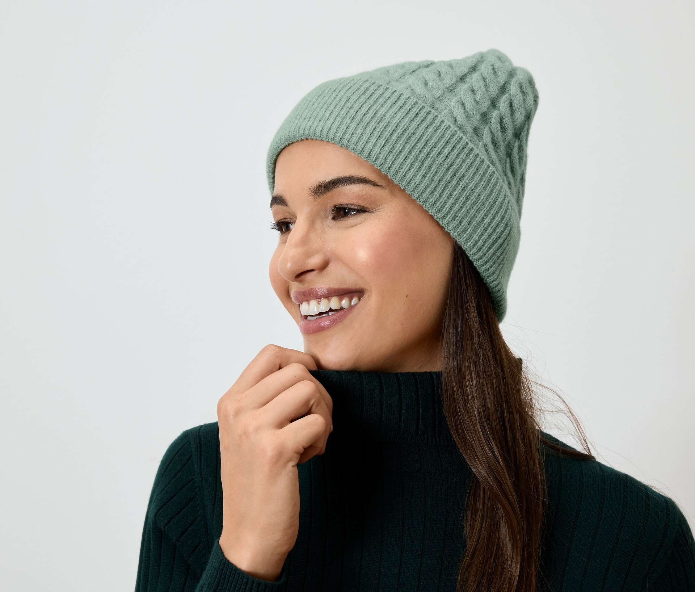 Uśmiechnięta kobieta z brązowymi włosami w zielonej czapce z dzianiny i zielonym golfie.