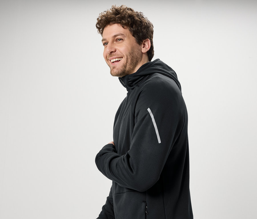 Uśmiechnięty mężczyzna z kręconymi włosami w czarnej bluzie z kapturem.