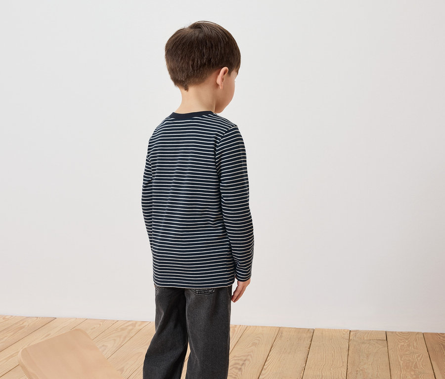 Chłopiec stoi tyłem, ubrany w koszulkę z długim rękawem w paski i dżinsy.