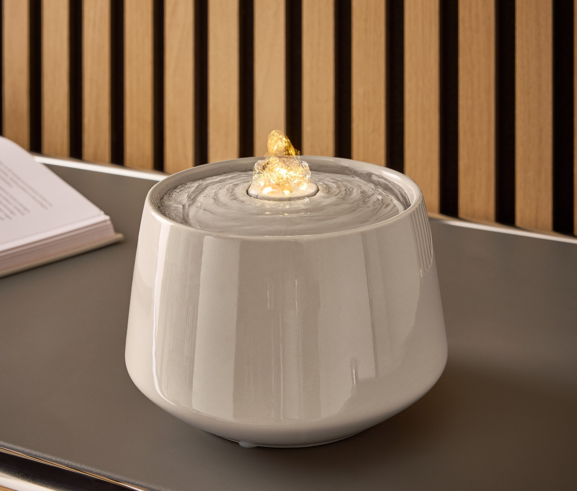 Szara ceramiczna fontanna z wodą i podświetlonym kamieniem na szarym stole.