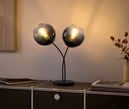 Dwie szklane lampy z żarówkami na czarnej komodzie.