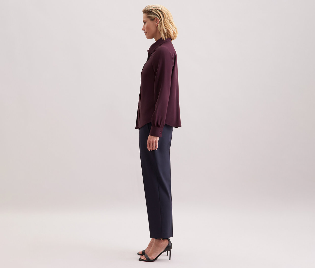 Kobieta ma na sobie bluzkę z wiskozy Seidensticker, ciemne spodnie i czarne sandały.