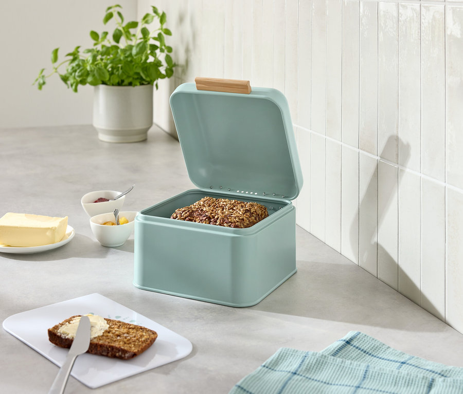 Otwarty, jasnoniebieski chlebak z chlebem, obok masło, dżem, nóż i posmarowany chleb.