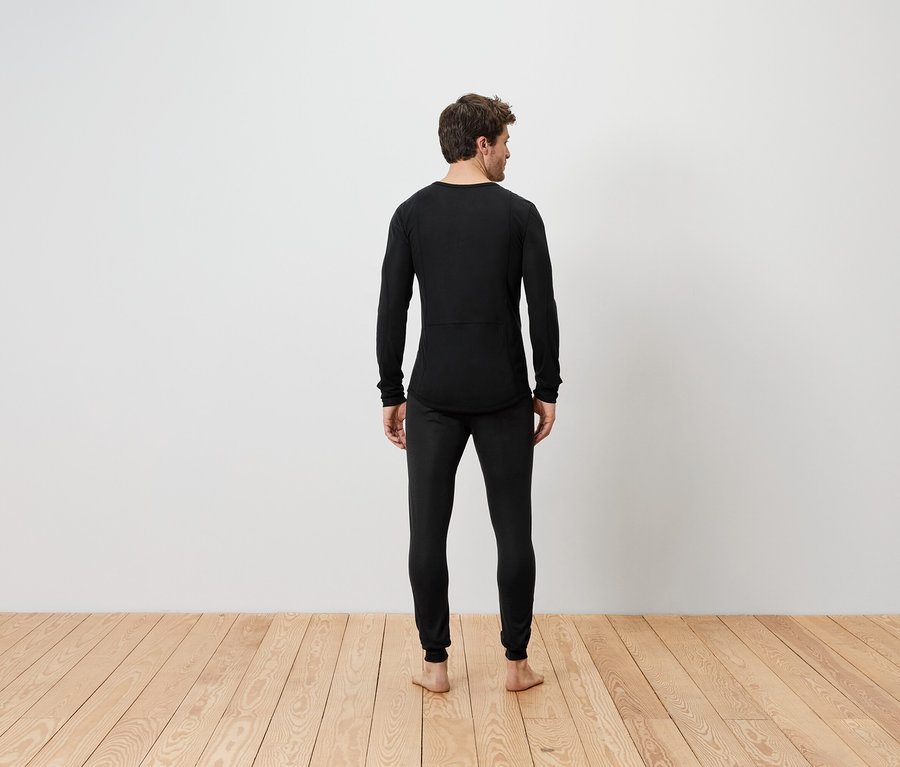 Mężczyzna stoi tyłem, ubrany w czarną bieliznę termiczną.