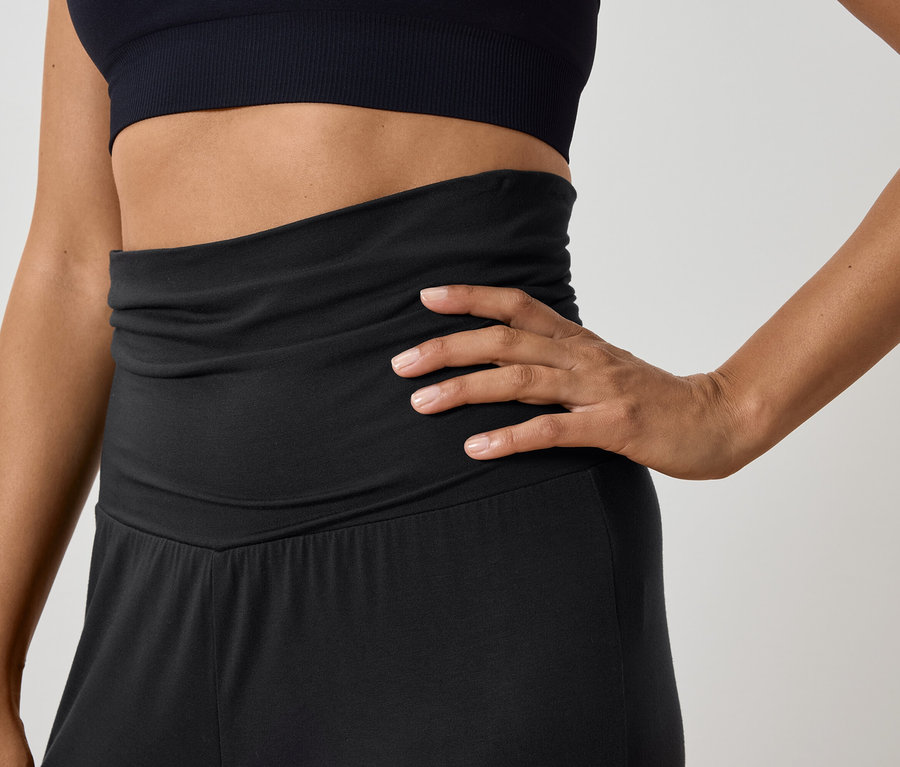 Kobieta pozuje w czarnym topie sportowym i spodniach z wysokim stanem.