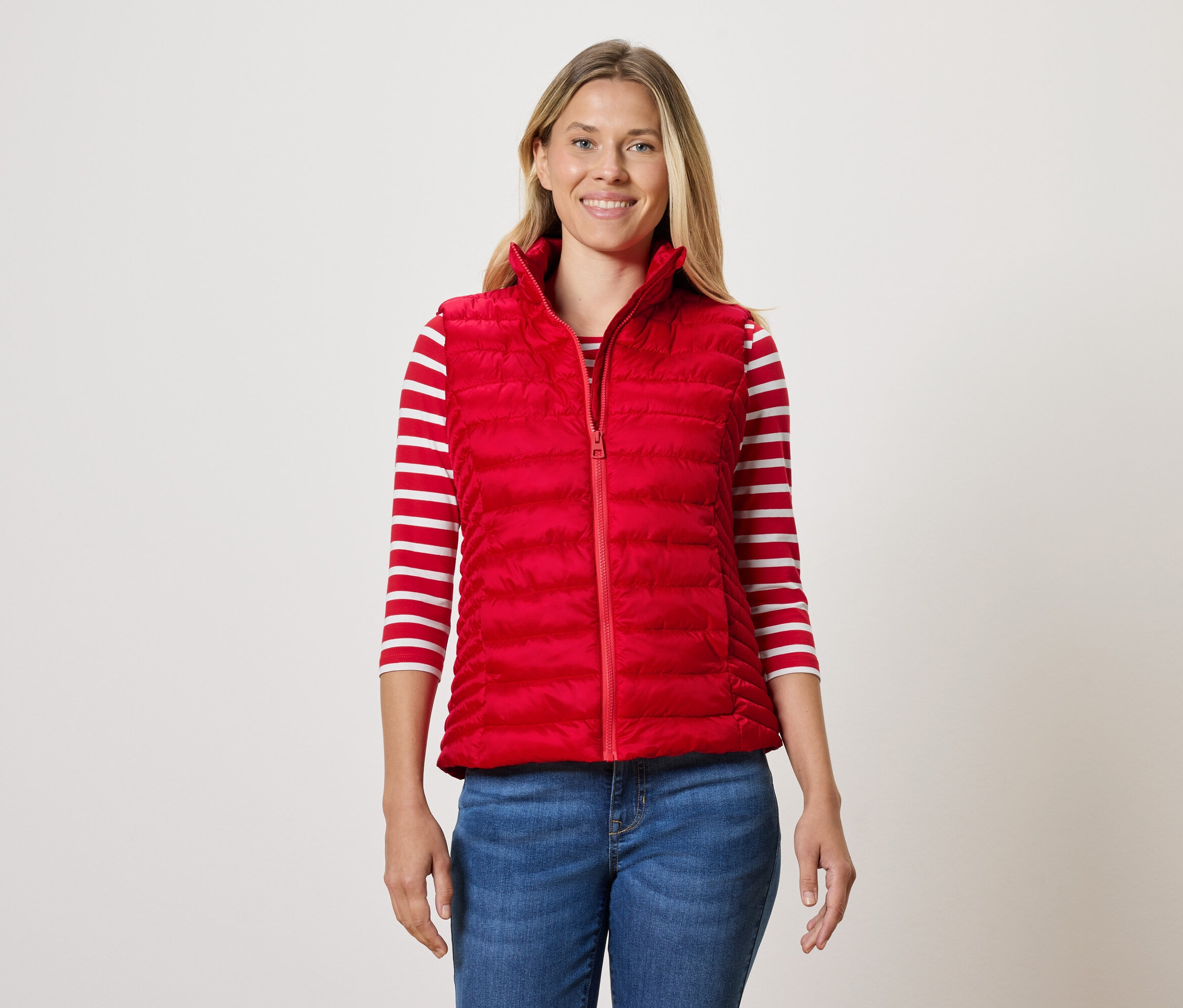 Kobieta ma na sobie czerwoną pikowaną kamizelkę, bluzkę w paski i dżinsy.