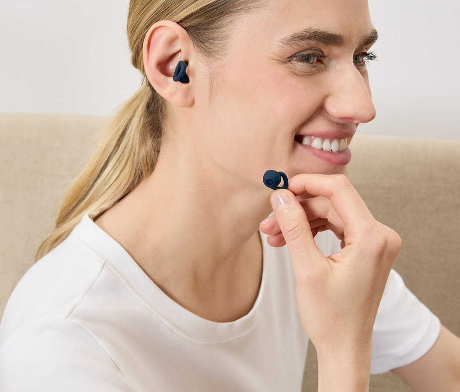 Kobieta wkłada ciemnoniebieską bezprzewodową słuchawkę do ucha.