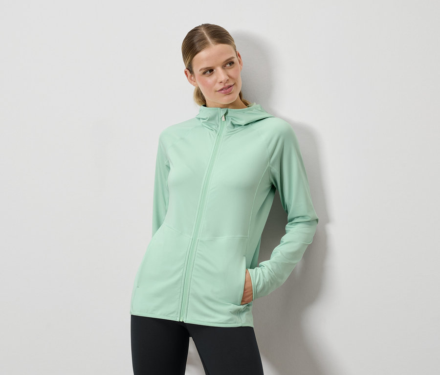 Kobieta pozuje w miętowo zielonej bluzie z kapturem i czarnych legginsach.