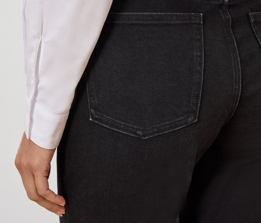 Zbliżenie na tył czarnych dżinsów na osobie w białej koszuli.