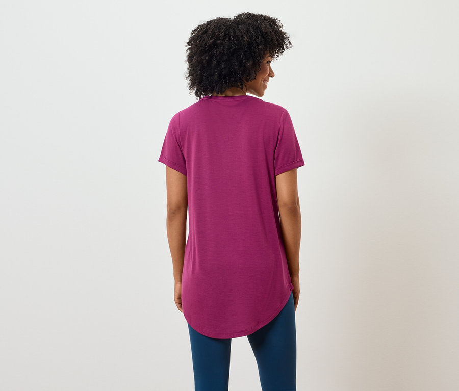 Widok z tyłu kobiety z ciemnymi, kręconymi włosami, ubranej w purpurowy T-shirt i niebieskie legginsy.