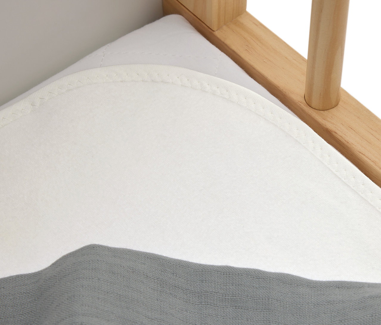 Zbliżenie na biały materac z szarą tkaniną na drewnianym łóżku.