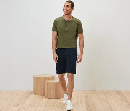Mężczyzna idzie ubrany w khaki t-shirt i granatowe szorty chinosy.