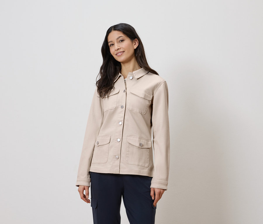 Kobieta ma na sobie beżową kurtkę i niebieskie spodnie.