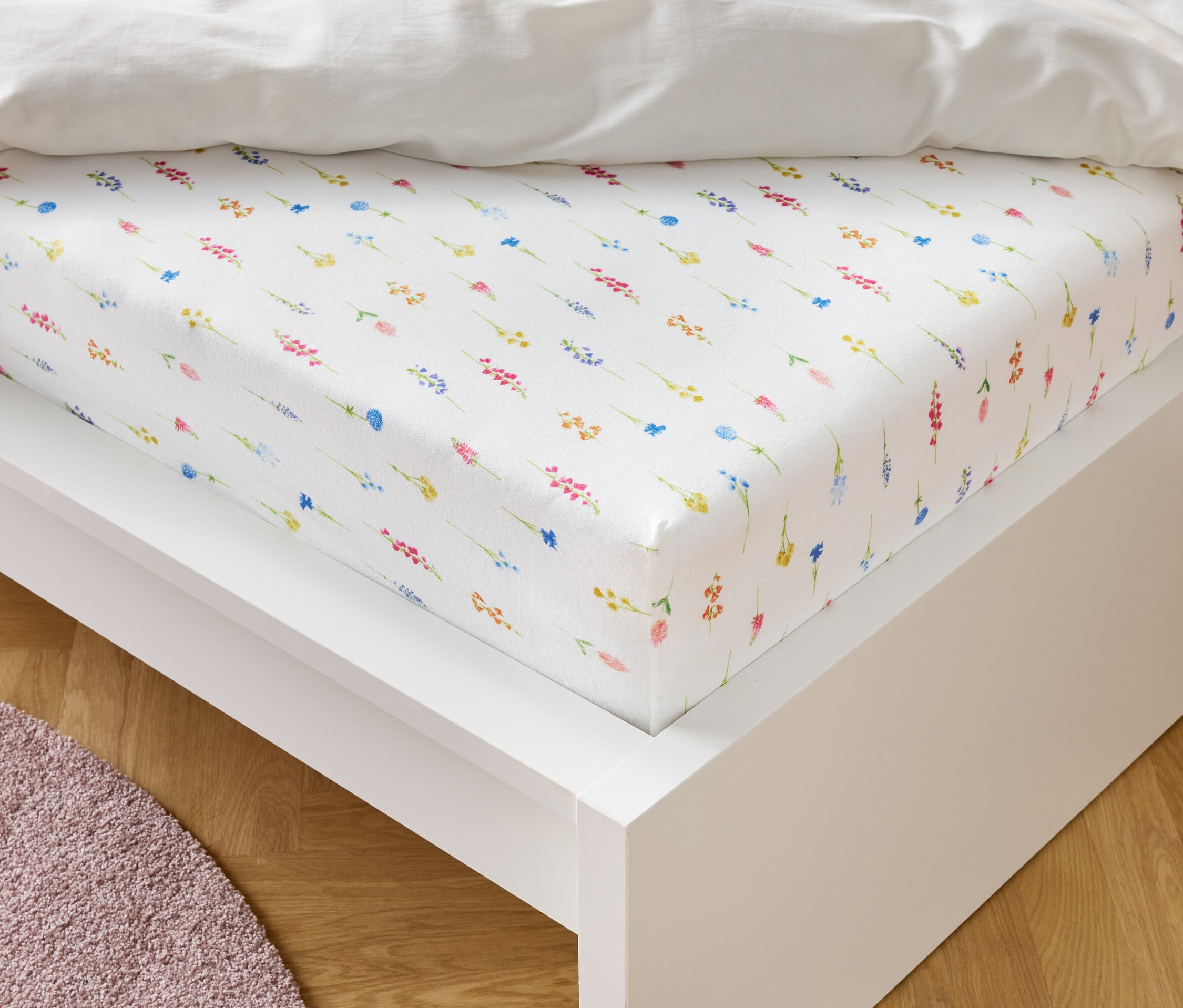 Białe prześcieradło z gumką w kwiatowy wzór leży na białej ramie łóżka.