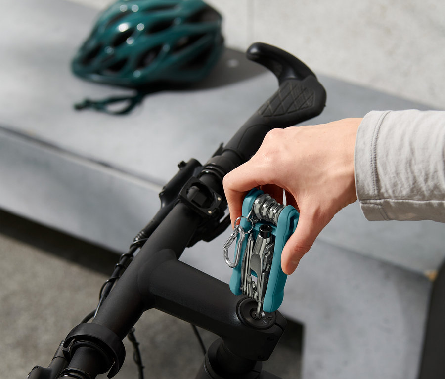 Ręka mocuje narzędzie wielofunkcyjne do kierownicy roweru, w tle kask rowerowy.