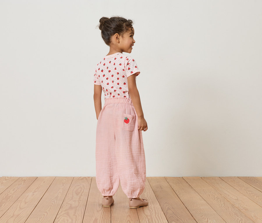 Dziewczynka od tyłu, ma na sobie koszulkę w truskawki i różowe spodnie z truskawkowym detalem.