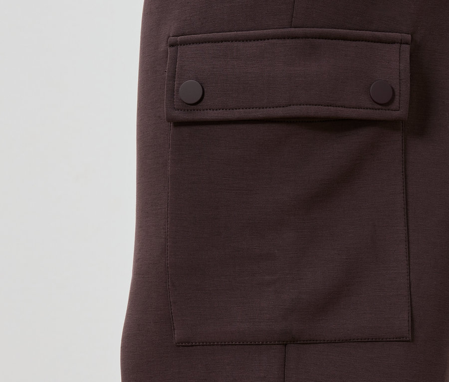 Szczegółowy widok kasztanowych spodni z naszytą kieszenią zapinaną na dwa okrągłe guziki.