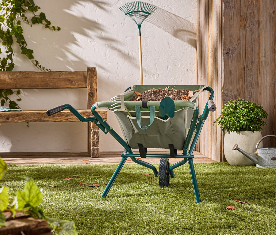 Zielony wózek stoi na trawniku z narzędziami ogrodniczymi w środku.