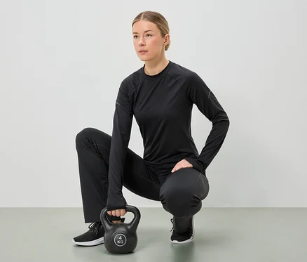 Kobieta w czarnym stroju sportowym kuca, trzymając oburącz 4-kilogramowy kettlebell.