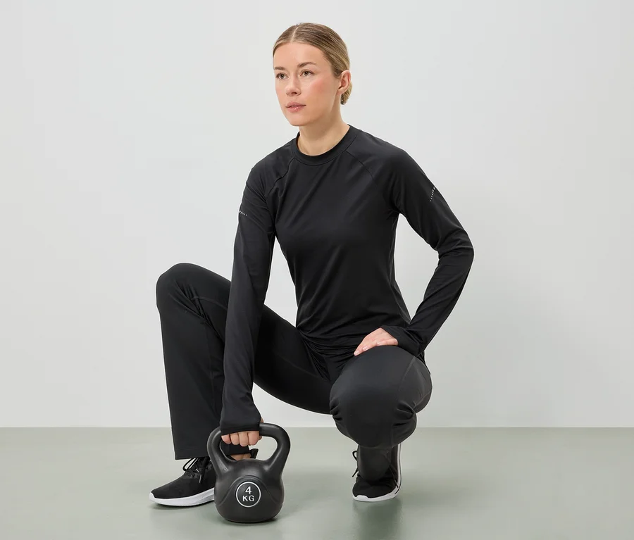 Kobieta w czarnym stroju sportowym kuca, trzymając oburącz 4-kilogramowy kettlebell.