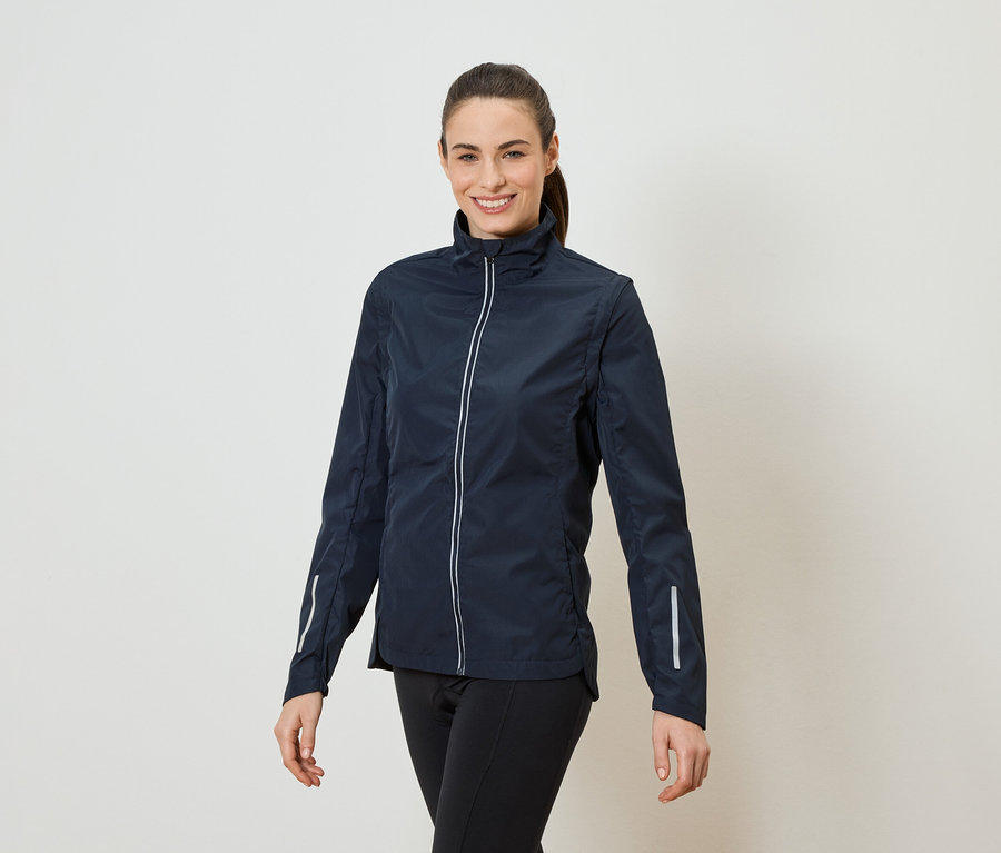 Kobieta z kucykiem ma na sobie granatową kurtkę zapinaną na zamek i czarne legginsy.