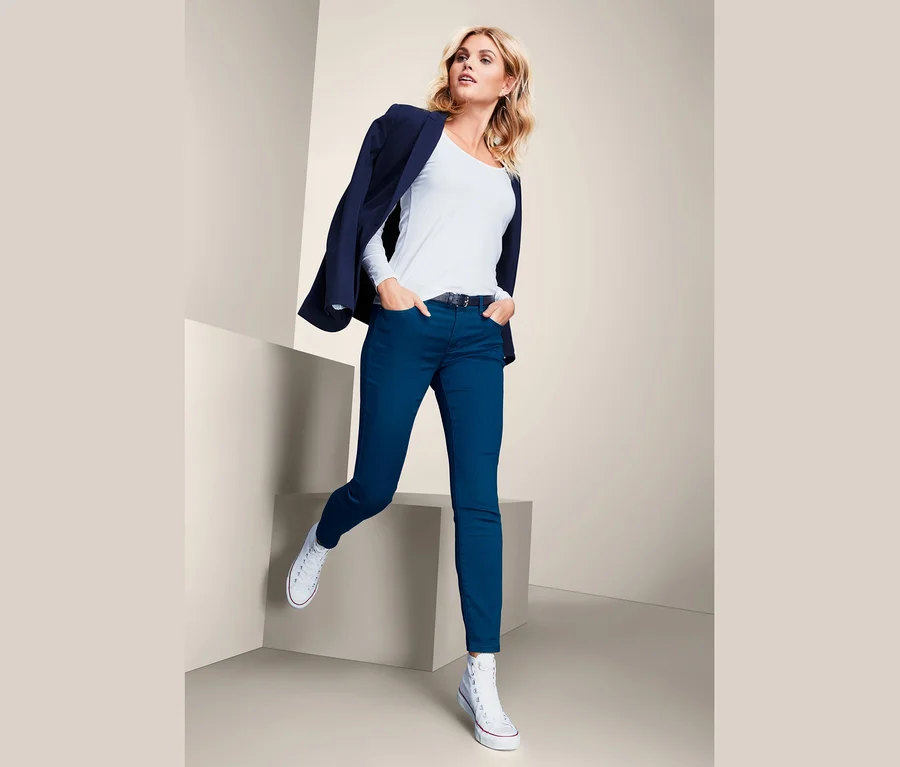 Blondynka pozuje w niebieskich spodniach slimfit, białym T-shircie i marynarce.