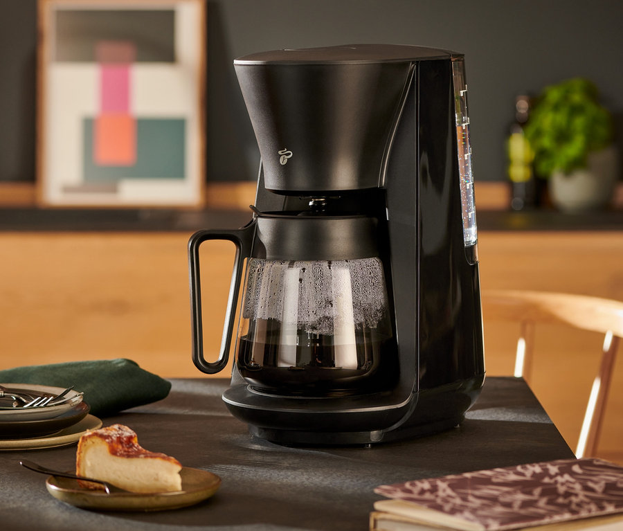 Czarny ekspres przelewowy »Let's Brew« na stole z kawą, ciastem i talerzami.
