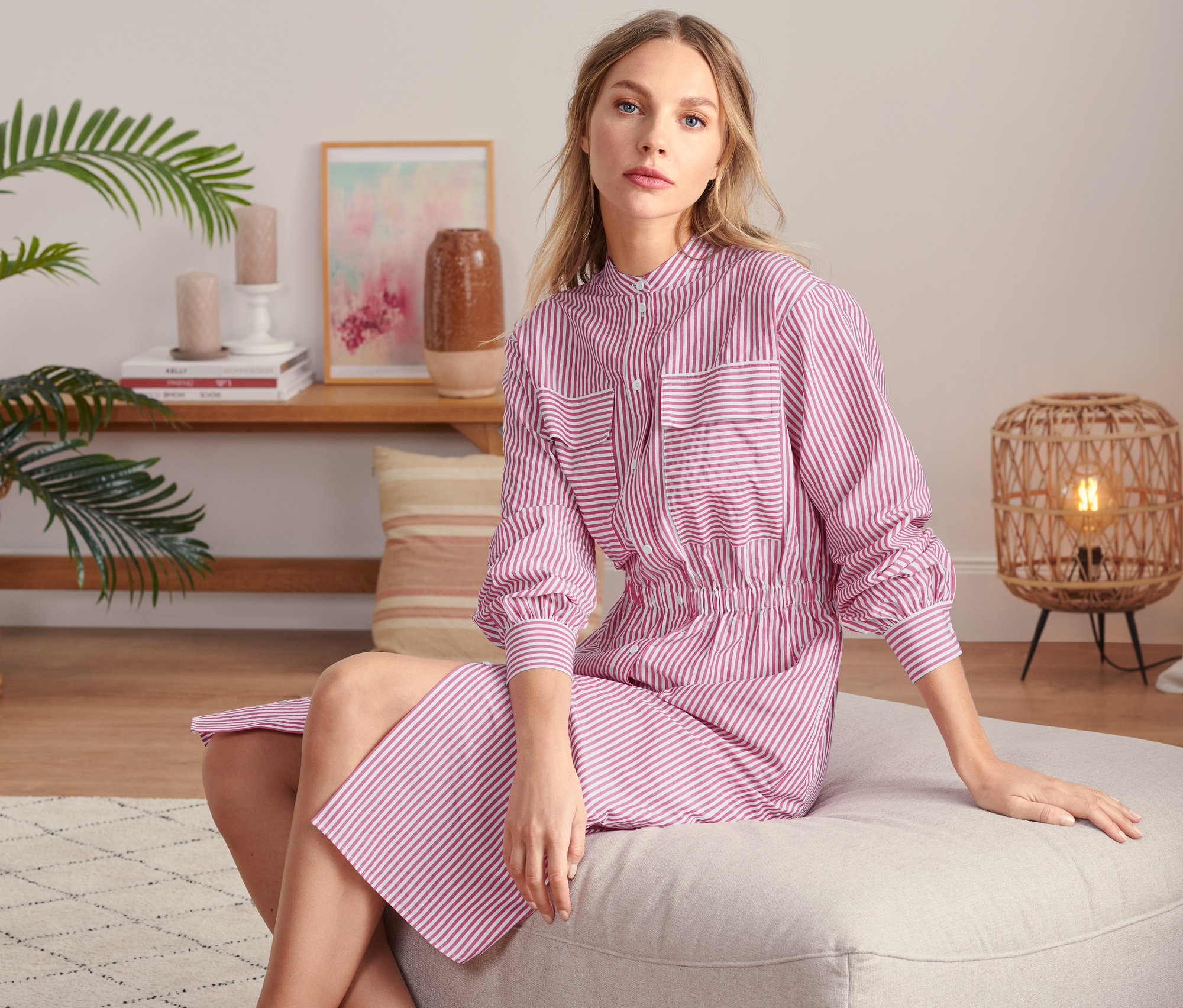 Kobieta siedzi w sukience koszulowej w paski.